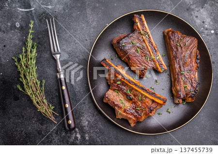 Gourmet glazed beef short ribs with fresh rosemary. Deep rusty brown background with ample negative space. Gourmet glazed beef short ribs with fresh rosemary. Deep rusty brown background with ample negative space. 137455739