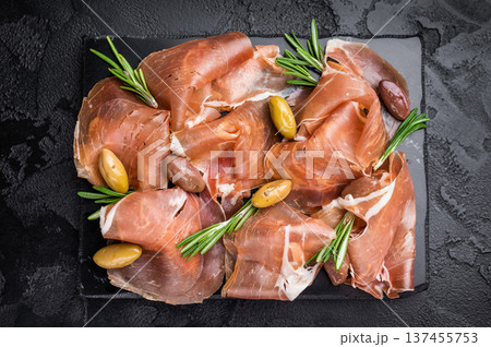 Appetizer of Sliced Ham and Olives garnished with rosemary, set on a dark rustic surface. Traditional Mediterranean snack. 137455753