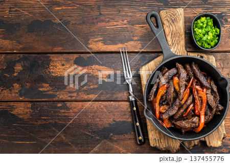 Beef stir fry with bell peppers cooked in cast iron skillet on rustic wooden table. Chinese pepper steak style dish with copy space. Beef stir fry with bell peppers cooked in cast iron skillet on rustic wooden table. Chinese pepper steak style dish with copy space. 137455776