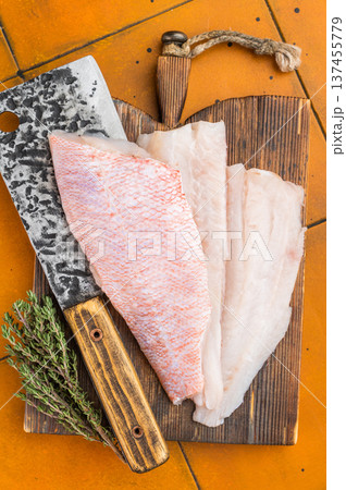 Raw rosefish or snapper fillets with herbs and cleaver on wooden board. Seafood preparation scene with bright background. 137455779
