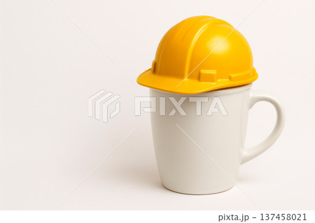 A white mug in a yellow construction helmet. Space for text. 137458021