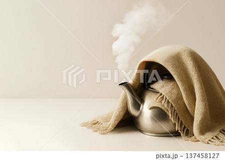 The kettle under the blanket releases steam. Space for text. 137458127