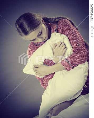 Sad depressed girl in bed gripping pillow 137458825