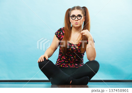 Happy teenage woman holding fake eyeglasses on stick 137458901