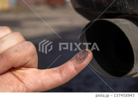 Mechanic points to carbon buildup in a car's exhaust pipe while performing maintenance in a workshop Mechanic points to carbon buildup in a car's exhaust pipe while performing maintenance in a workshop 137458943