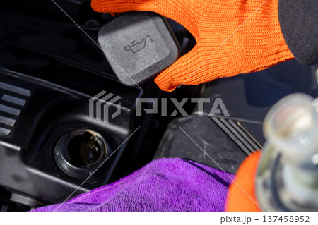 A mechanic holds an engine cover above the engine bay. He works on a vehicle in a garage during daylight hours 137458952