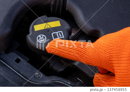 A mechanic points at the radiator cap to explain its location and function while working in a garage on a bright day 137458955