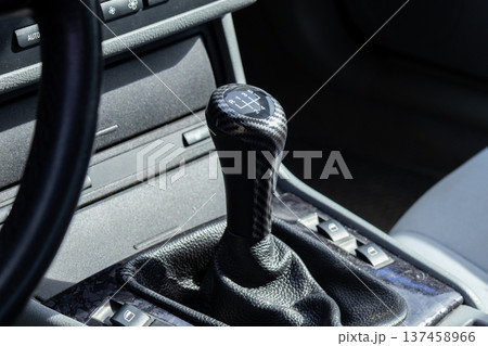 A car interior shows the gear shift in the center console, with dashboard buttons and controls nearby. The setting is a contemporary vehicle 137458966