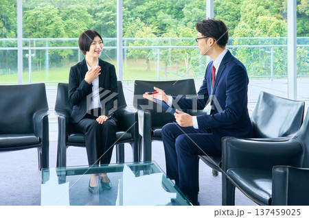 明るいオフィスのロビーで採用面接を受けるリクルートスーツの女性と面接官のビジネスマ 137459025