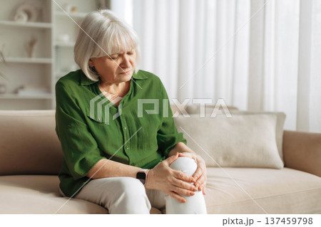 Senior woman holding painful knee while sitting on sofa at home 137459798