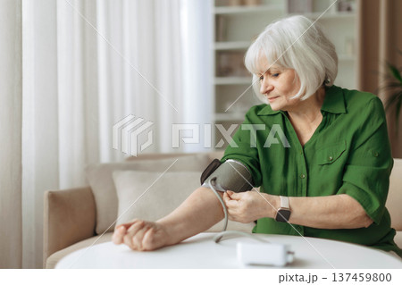 Senior woman adjusting blood pressure cuff on arm while sitting at home Senior woman adjusting blood pressure cuff on arm while sitting at home 137459800