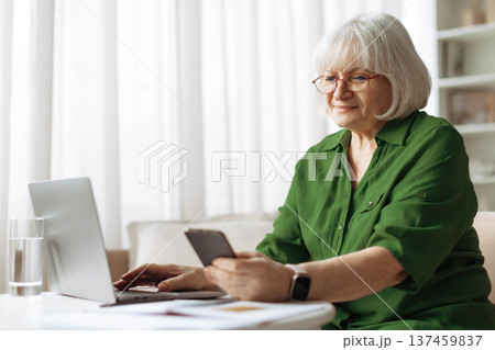 Senior woman using smartphone and laptop at home while checking online information Senior woman using smartphone and laptop at home while checking online information 137459837