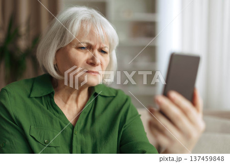 Senior woman squinting eyes while looking at smartphone screen Senior woman squinting eyes while looking at smartphone screen 137459848