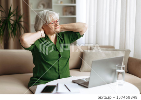 Senior woman stretching neck and shoulders after using laptop at home Senior woman stretching neck and shoulders after using laptop at home 137459849