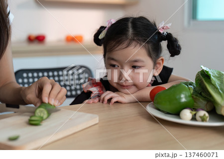 A young girl is sitting at a table with a woman, cutting up vegetables A young girl is sitting at a table with a woman, cutting up vegetables 137460071