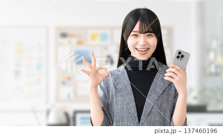 スマートフォンを持ってOKポーズをする若い女性・ビジネスウーマン スマートフォンを持ってOKポーズをする若い女性・ビジネスウーマン 137460196