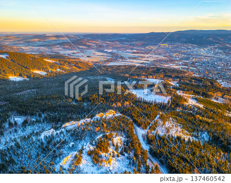 Aerial view shows a winter morning landscape in Liberec. Snow covers trees and fields. The sunlight creates shadows across the mountains and town below. Aerial view shows a winter morning landscape in Liberec. Snow covers trees and fields. The sunlight creates shadows across the mountains and town below. 137460542