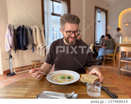 Man holding spoon and eating soup in cafe. Friendly dining moment, casual lifestyle, lunchtime atmosphere and relaxed urban restaurant scene. Man holding spoon and eating soup in cafe. Friendly dining moment, casual lifestyle, lunchtime atmosphere and relaxed urban restaurant scene. 137460614