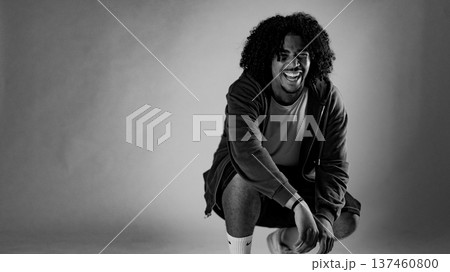 Young african-american man with curly hair squatting and laughing in black and white Young african-american man with curly hair squatting and laughing in black and white 137460800
