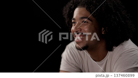 Young african-american man with curly hair smiling and looking away on black background Young african-american man with curly hair smiling and looking away on black background 137460899