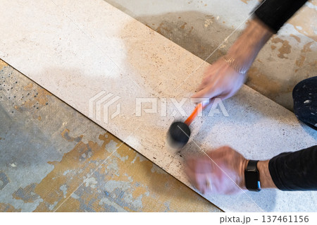 worker is gluing cork tiles with plastic hammer worker is gluing cork tiles with plastic hammer 137461156
