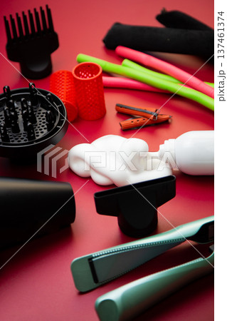 Close-up side view on a pink background, hairdryer with attachments, stylers and curling irons for straightening and creating curls, foam for volume and long-lasting, curlers in different shapes and Close-up side view on a pink background, hairdryer with attachments, stylers and curling irons for straightening and creating curls, foam for volume and long-lasting, curlers in different shapes and 137461374