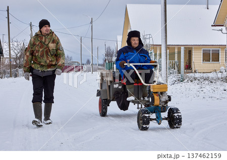 Walk behind tractor used by farmers to transport cargo inside trailer during winter season in rural area. 137462159