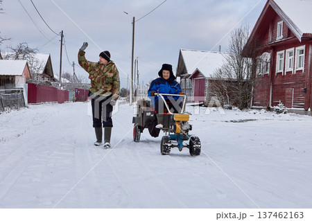Two wheel tractor with trailer used by two farmers to move loads in snowy winter village. Two wheel tractor with trailer used by two farmers to move loads in snowy winter village. 137462163