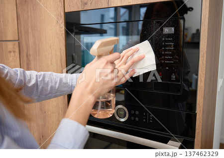 Hands spray and wipe glass door of built in microwave oven in kitchen cabinet 137462329