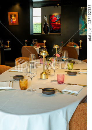 Elegant dining arrangement. Stylish communal dining table featuring brass lamps and floral accents Elegant dining arrangement. Stylish communal dining table featuring brass lamps and floral accents 137462588
