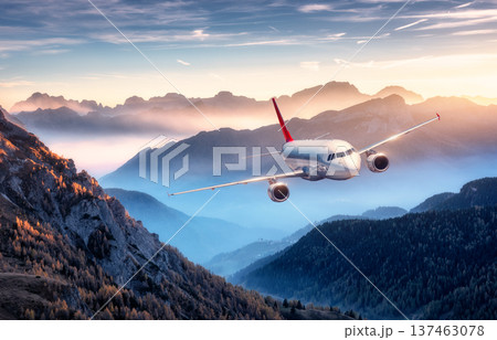 Commercial airplane flying over mountain peaks in fog at sunset Commercial airplane flying over mountain peaks in fog at sunset 137463078