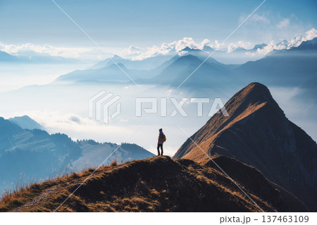 Woman with backpack standing on a mountain ridge above clouds 137463109