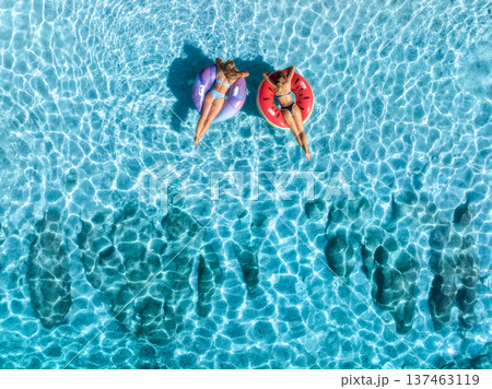Aerial view of beautiful young women on swim rings in blue sea Aerial view of beautiful young women on swim rings in blue sea 137463119