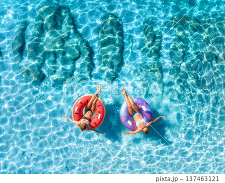 Aerial view of beautiful young women on swim rings in blue sea Aerial view of beautiful young women on swim rings in blue sea 137463121