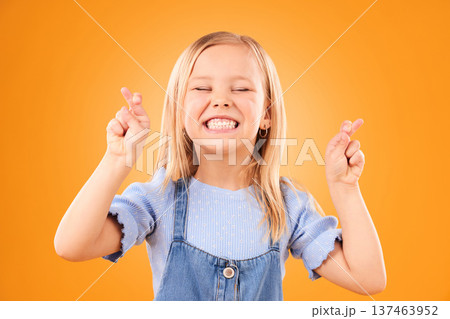 Child, fingers crossed and wish or hope in studio for luck, prayer or faith. Face of excited young girl kid on a orange background for hand gesture, icon or sign for dream, optimistic or superstition Child, fingers crossed and wish or hope in studio for luck, prayer or faith. Face of excited young girl kid on a orange background for hand gesture, icon or sign for dream, optimistic or superstition 137463952