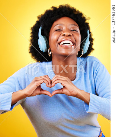 Portrait, heart hands and headphones of woman in studio for sign, kindness or thank you on yellow background. Happy african model, finger shape or icon of hope, love or emoji while listening to music Portrait, heart hands and headphones of woman in studio for sign, kindness or thank you on yellow background. Happy african model, finger shape or icon of hope, love or emoji while listening to music 137463961