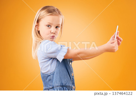 Phone, selfie or portrait of child in studio with confidence or mockup space in photograph memory. Kid, orange background or face of girl taking picture online on a social media app on internet Phone, selfie or portrait of child in studio with confidence or mockup space in photograph memory. Kid, orange background or face of girl taking picture online on a social media app on internet 137464122