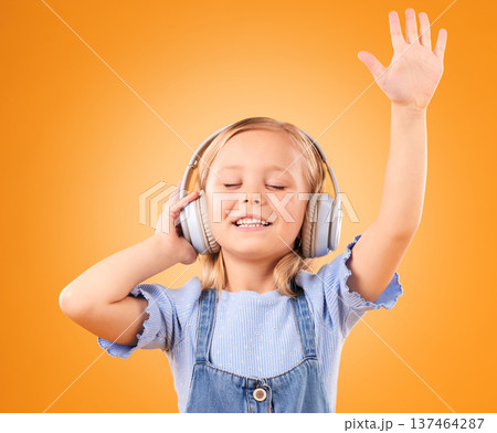 Headphones, happy or child streaming music to relax with freedom in studio on orange background. Hand up, singing or girl singer listening to a radio song, sound or gospel on an online subscription Headphones, happy or child streaming music to relax with freedom in studio on orange background. Hand up, singing or girl singer listening to a radio song, sound or gospel on an online subscription 137464287