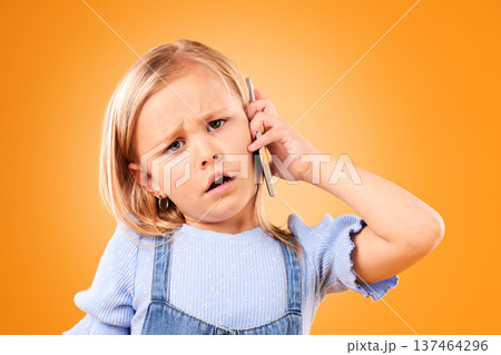 Portrait, phone and a confused girl on an orange background in studio for a communication question. Face, mobile and doubt with a young female child looking unsure while chatting or speaking 137464296