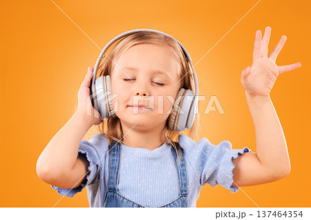 Child, headphones and dance to music in studio for freedom, multimedia subscription or kids podcast on orange background. Happy young girl listening to audio, streaming sound or hearing song on radio 137464354