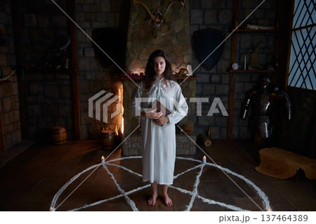 Caucasian woman standing inside pentagram circle, candlelit medieval chamber 137464389