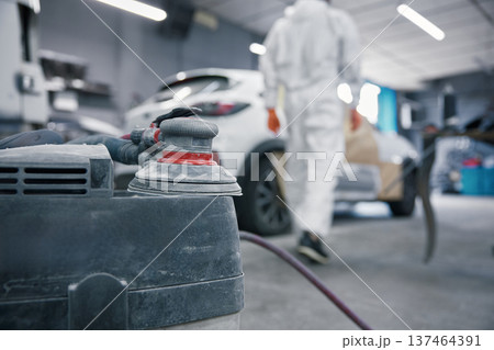 Auto body shop car painting prep with orbital sander and technician in protective suit 137464391