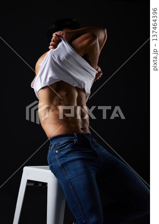 Fitness, body and man on chair remove tshirt for wellness and workout in studio on black background. Bodybuilder, strong and person show stomach for motivation, muscle and lifestyle with pride Fitness, body and man on chair remove tshirt for wellness and workout in studio on black background. Bodybuilder, strong and person show stomach for motivation, muscle and lifestyle with pride 137464396