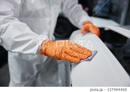 Automotive technician sanding car body panel with orange gloves and protective coverall 137464408