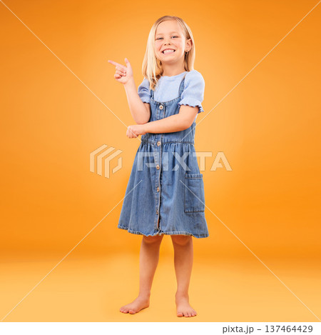 Pointing, happy portrait and child in studio for advertising, announcement or promotion. Excited barefoot girl kid on a orange background for hand gesture, sale or sign for mockup space or fashion Pointing, happy portrait and child in studio for advertising, announcement or promotion. Excited barefoot girl kid on a orange background for hand gesture, sale or sign for mockup space or fashion 137464429