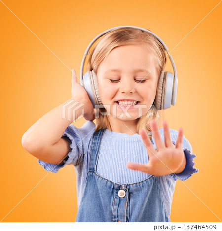 Headphones, dancing or child streaming music to relax with freedom in studio on orange background. Smile, excited and happy girl listening to a radio song, sound or audio on an online subscription Headphones, dancing or child streaming music to relax with freedom in studio on orange background. Smile, excited and happy girl listening to a radio song, sound or audio on an online subscription 137464509