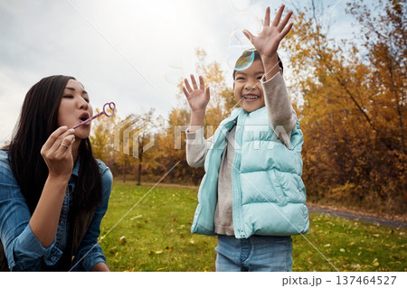 Asian, daughter or mom blowing with bubbles in park for playful childhood or outdoor bonding. Mother, child or kid with wand for parenting, development or fun magical moments together in nature 137464527