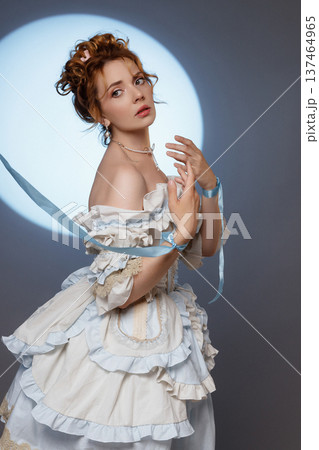 Young woman in ornate Rococo dress holding blue rope against full moon background 137464965