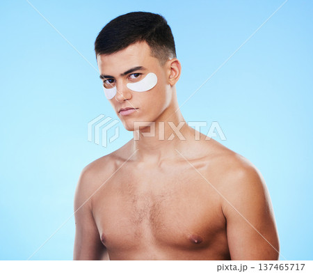 Man, beauty and portrait with eye patch for skincare, grooming and clean with hygiene on blue background. Skin treatment, cosmetics product and wellness, self care and dermatology in a studio Man, beauty and portrait with eye patch for skincare, grooming and clean with hygiene on blue background. Skin treatment, cosmetics product and wellness, self care and dermatology in a studio 137465717