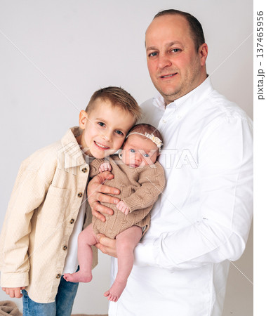 Father holding a newborn baby while standing next to his young son. Warm family portrait showing parenting, sibling relationship and love between family members. Concept of fatherhood and happy family Father holding a newborn baby while standing next to his young son. Warm family portrait showing parenting, sibling relationship and love between family members. Concept of fatherhood and happy family 137465956